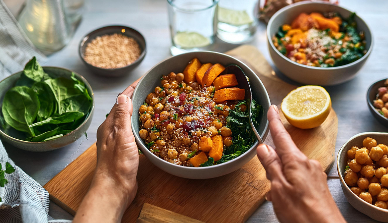 Hands serving a bowl of chickpeas, sweet potato, kale and quinoa