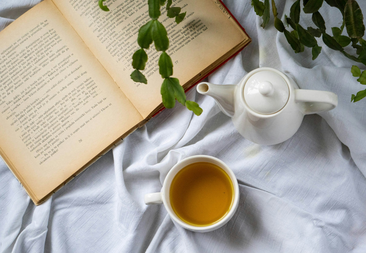 An open book and a cup of tea resting on a bed